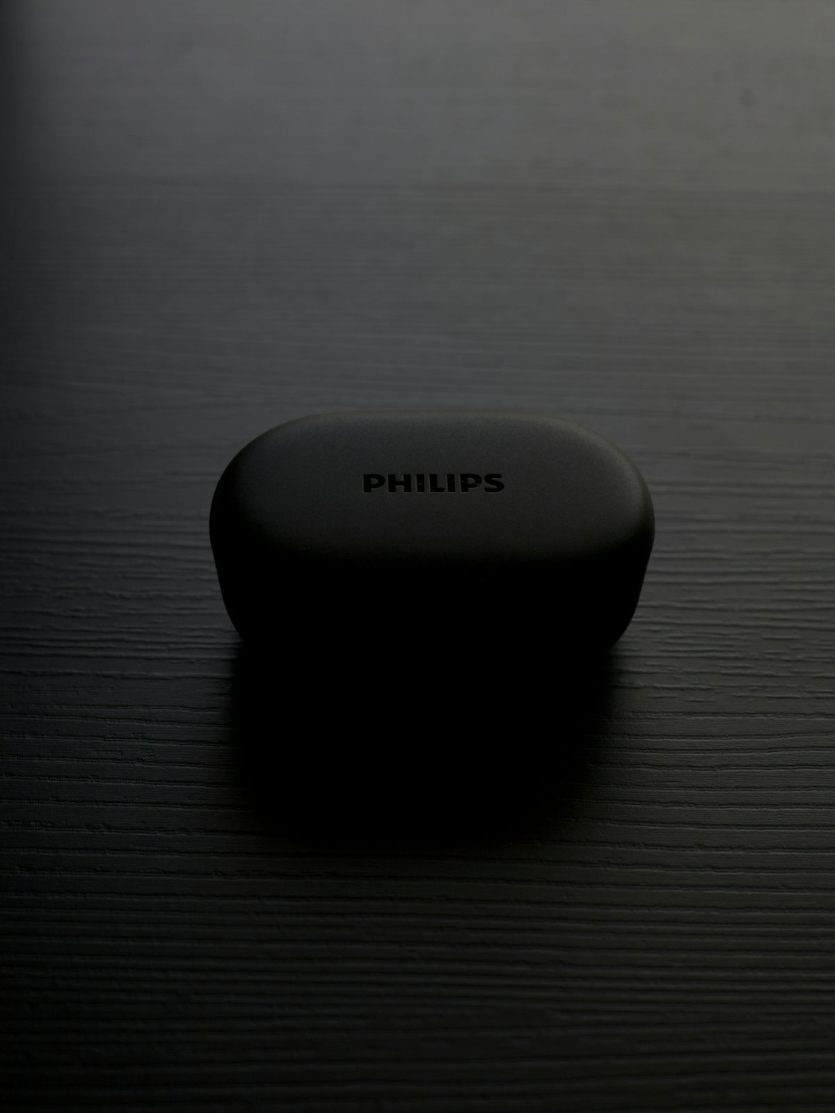 A philips earbuds case sits on a dark surface.