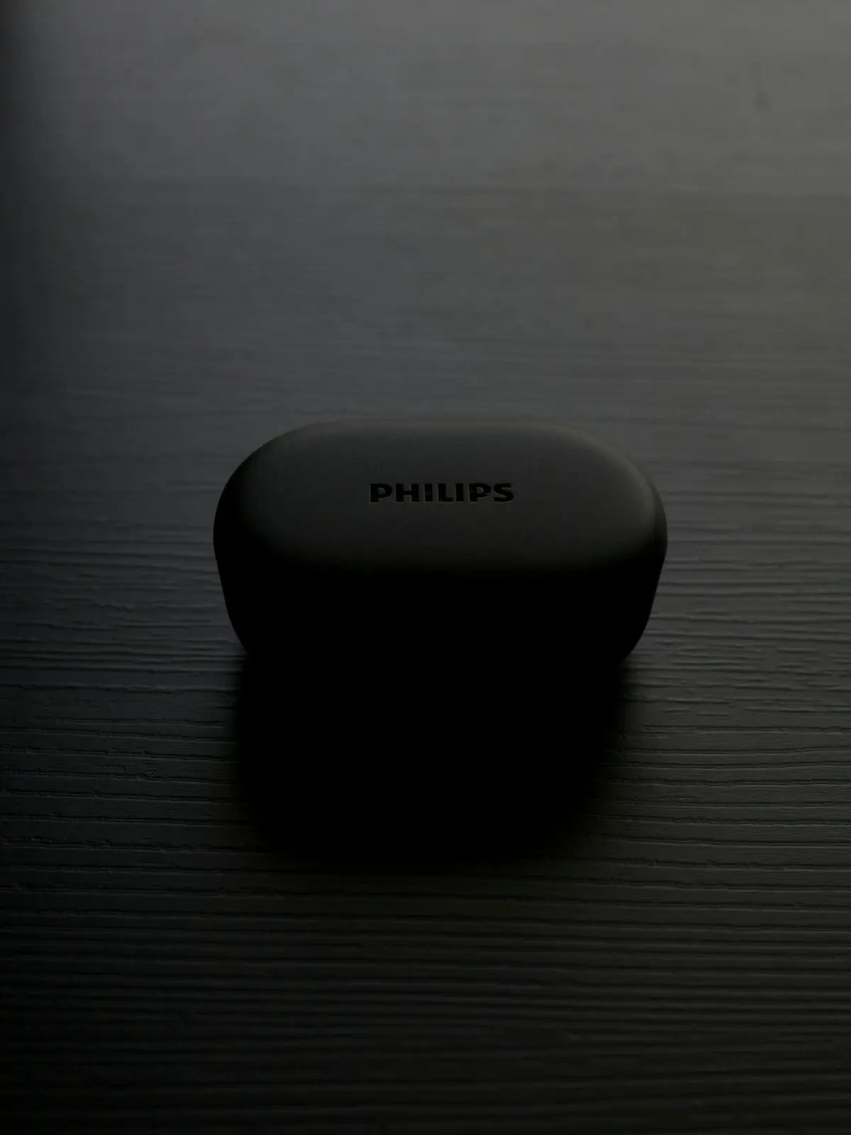 A philips earbuds case sits on a dark surface.